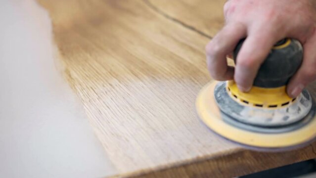 Trendy tabletop made of wooden slabs and white pearl colour epoxy resin, carpenter polishing tabletop with grinder machine to make it smooth and brilliant, work with wood and epoxy resin in workshop