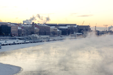 Obraz premium Steam coming from a frozen river near the embankment with residential houses