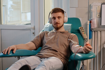 Portrait of serious caucasian man sitting in medical center and donating blood looking at camera