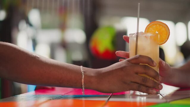 Bartender serves cocktail for guest in bar closeup. African American man pushes glass with exotic beverage to young woman tourist. Barman serves drink