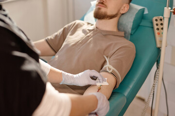 Obraz premium Nurse in protective gloves pulling out needle from arm of donor after taking his blood sample
