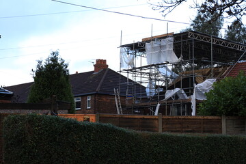 Storm damage: Large house with scaffolding on roof, surrounded by wood and brick buildings