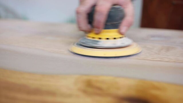 Wooden tabletop with white pearl colour epoxy resin long strip, craftsman polishing table surface with electrical grinder machine, process of smoothing wooden surface, manufacturing concept