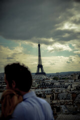 Loving couple embraces looking at the Eiffel Tower in Paris under a romantic sunset in the city of lovers in 2023
​