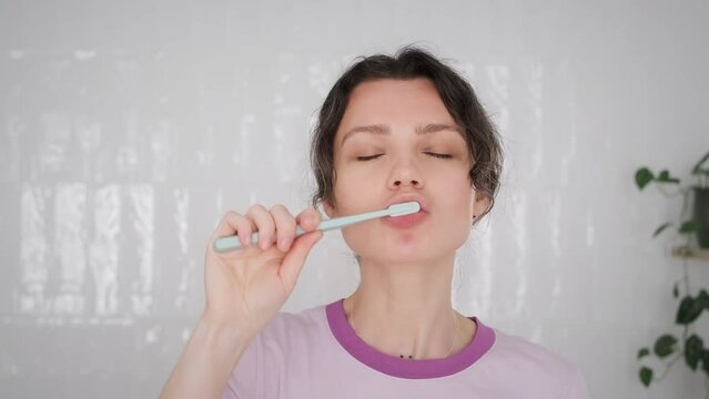 young woman brushes her teeth in her light white bathtub with toothbrush made from recycled plastic. do morning routine with pleasure. Life without depression. Happy morning. close up portrait