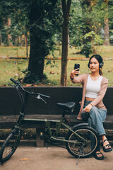 Naklejka premium Happy young Asian woman while riding a bicycle in a city park. She smiled using the bicycle of transportation. Environmentally friendly concept.