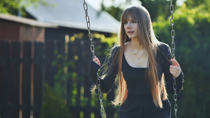 A blonde-haired girl in a black dress rides on a swing.