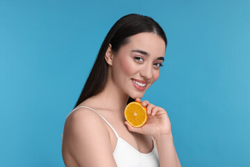Obraz na płótnie Canvas Beautiful young woman with piece of orange on light blue background