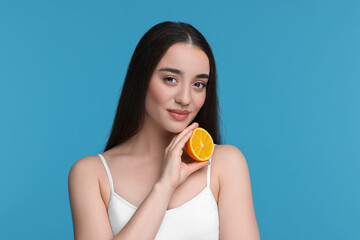 Beautiful young woman with piece of orange on light blue background
