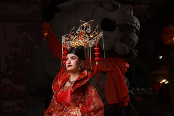 A charming Asian woman in Red ancient Chinese costume with a lion statue at a shrine