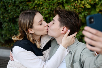 Fototapeta premium young people take a selfie on their phone while kissing in the park