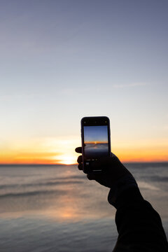 Person at sunrise at sea taking pictures with mobile phone