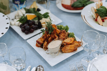 A view of wedding tables, attention to serving, with flower arrangements, expensive cutlery, plates with white napkins.