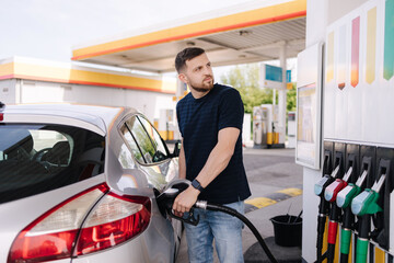 Fototapeta na wymiar Bearded man refuelling car on gas station and looking into his smartphone. Man compares fuel prices 