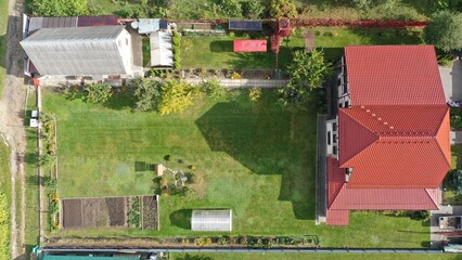 Private fenced area with a house, bathhouse, barn, well, garden of fruit trees and shrubs, ornamental green grass for playing soccer with a goal. View vertically from above, aerial view.