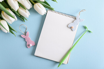 Floral border from bouquet of white tulips, Easter eggs and blank notebook on blue background. Easter celebration concept. Copy space. Top view