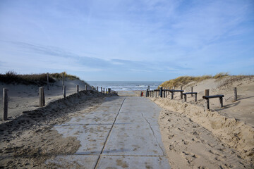 concrete path to the beach between the dunes to the lovely sea, with sun and blue sky