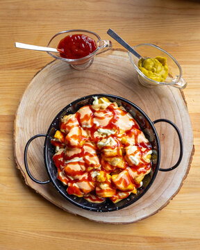 Vista cenital de un sabroso plato de patatas bravas, acompa&ntilde;adas de salsa de tomate y guacamole, en la mesa de madera de un restaurante