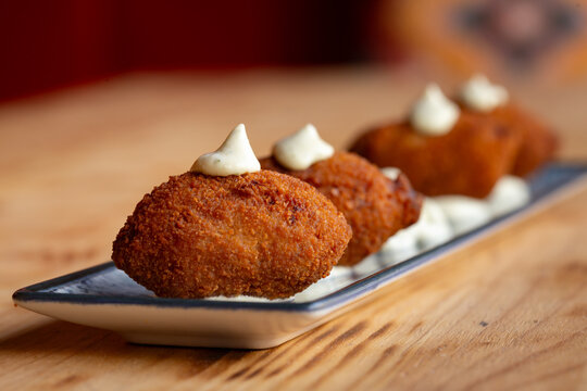 Plato de apetitosas croquetas con salsa mayonesa y ali oli en la mesa de madera de un restaurante espa&ntilde;ol