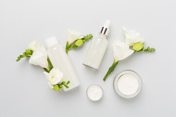 Fototapeta na wymiar Facial cosmetic products with freesia flowers on color background, top view