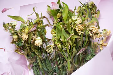 A bouquet with dried flowers lies on pink wrapping paper close-up, wilted flowers