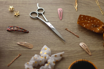 Fototapeta na wymiar Wooden hairbrush, scissors and various headbands, hair clips and scrunchies on wooden background. Selective focus.