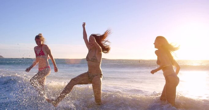 Friends, women and playing in ocean at sunset, freedom and bonding on weekend social trip. People, crazy fun and happiness in nature or traveling on vacation, holiday and love on outdoor adventure