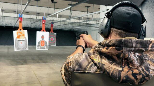 Man Practicing Shooting at Indoor Range, Person in camo attire aiming a handgun at targets in a shooting range, focusing on precision and safety.