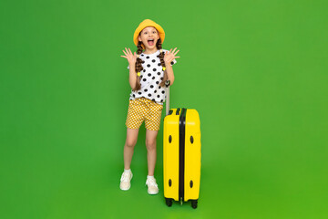 A little girl gathered with a large yellow suitcase for a children's holiday camp. A child dressed in a hat and shorts in anticipation of a big trip. Green isolated background.