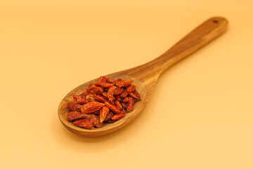 photograph of a wooden spoon with dried cayenne peppers or capsicum annuum on orange background with copy space