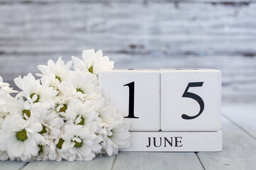 World Elder Abuse Awareness Day. White wood calendar blocks with the date June 15th and white daisies. Selective focus with blurred background. 