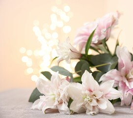 Bouquet of beautiful lily flowers on table against beige background with blurred lights, closeup
