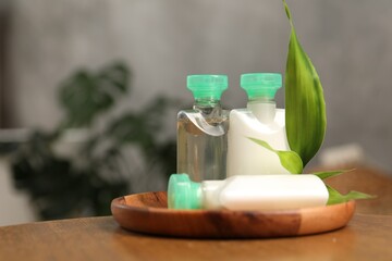 Mini bottles of cosmetic products and green branch on wooden table against blurred background. Space for text
