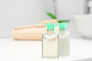 Mini bottles of cosmetic products on white table against blurred background. Space for text