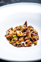 Setas de temporada salteadas  con yema de huevo curada con salsa de soja y flores decorativas sobre un plato de loza blanco