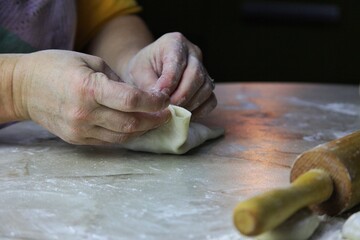 on the  table there is a flat pancake made of raw dough and in the center there is a pile of minced beef with onions. female hands wrap the edges for steaming manti dumplings. cooking homemade food