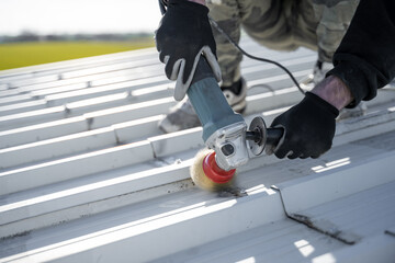 Worker removing rust from white metal roof with grinder. Technician repairing roof with professional tooling.  Roofing job and maintenance. Professional roofer.