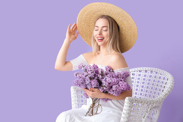 Young woman with lilac flowers in armchair on color background