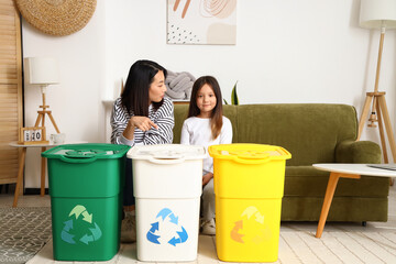 Asian mother with her little daughter and recycle bins at home