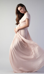 Fototapeta na wymiar Beautiful pregnant woman hugging her tummy. Woman in dress holding her belly gently standing on white background.