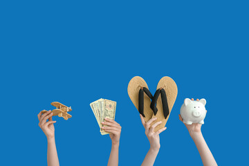 Female hands with wooden airplane, money, flip flops and piggy bank on blue background. Travel concept