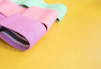 Set of bright multi-colored rubber bands for fitness on yellow background. Sports concept. Fitness trend. Top view, flat lay, copy space.