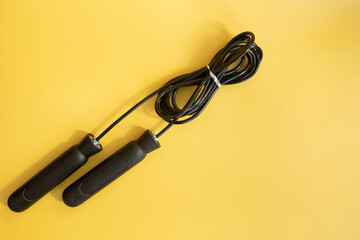Skipping rope with black handles on the yellow background. 