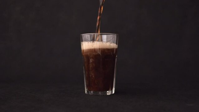Pouring cola into a glass. Filling a tall glass with dark liquid.