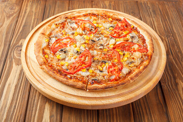 delicious pizza with chicken, mushrooms, cheese, tomatoes and corn on a wooden background