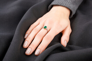 Beautiful female hand with gold ring with diamonds and emerald on gray background