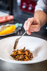 Chef prepara setas de temporada salteadas con yema de huevo curada con salsa de soja y flores decorativas sobre un plato de loza blanco