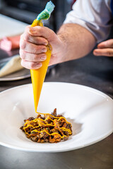 Chef prepara setas de temporada salteadas con yema de huevo curada con salsa de soja y flores decorativas sobre un plato de loza blanco