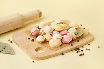 Wooden board of colorful raw dumplings with peppercorn and bay leaves on yellow background
