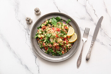 Plate with delicious tabbouleh salad and cutlery on light background